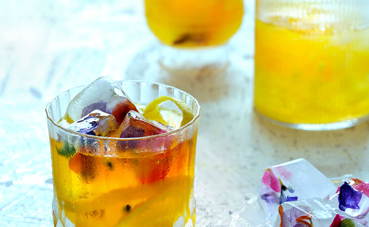 Golden passionfruit mocktail in glass tumblers with colourful ice cubes, perfect summer non-alcoholic drink.